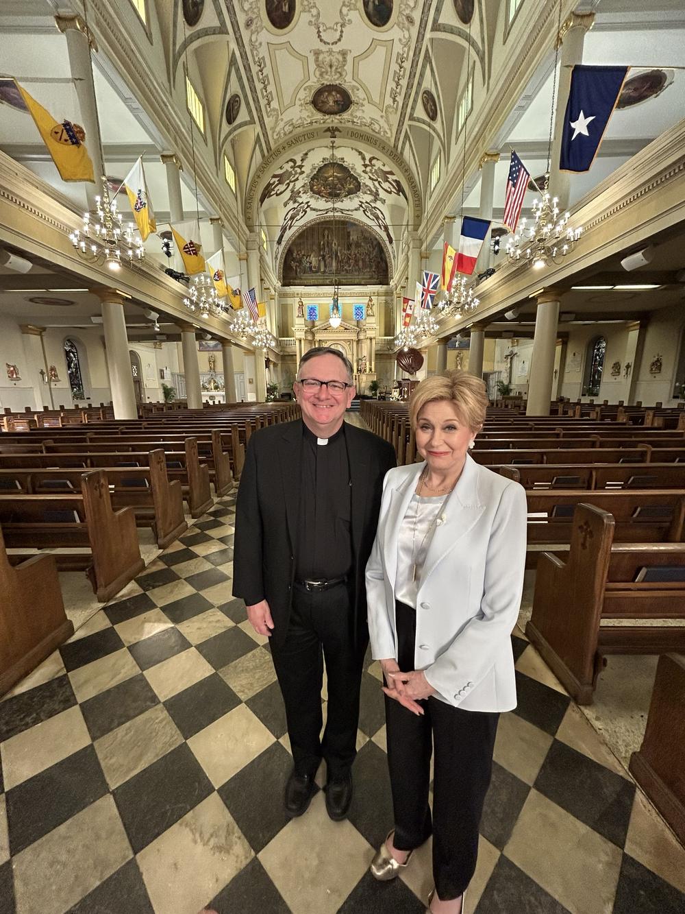 A priest and a guest stand in the empty nave on the checkerboard marble floor