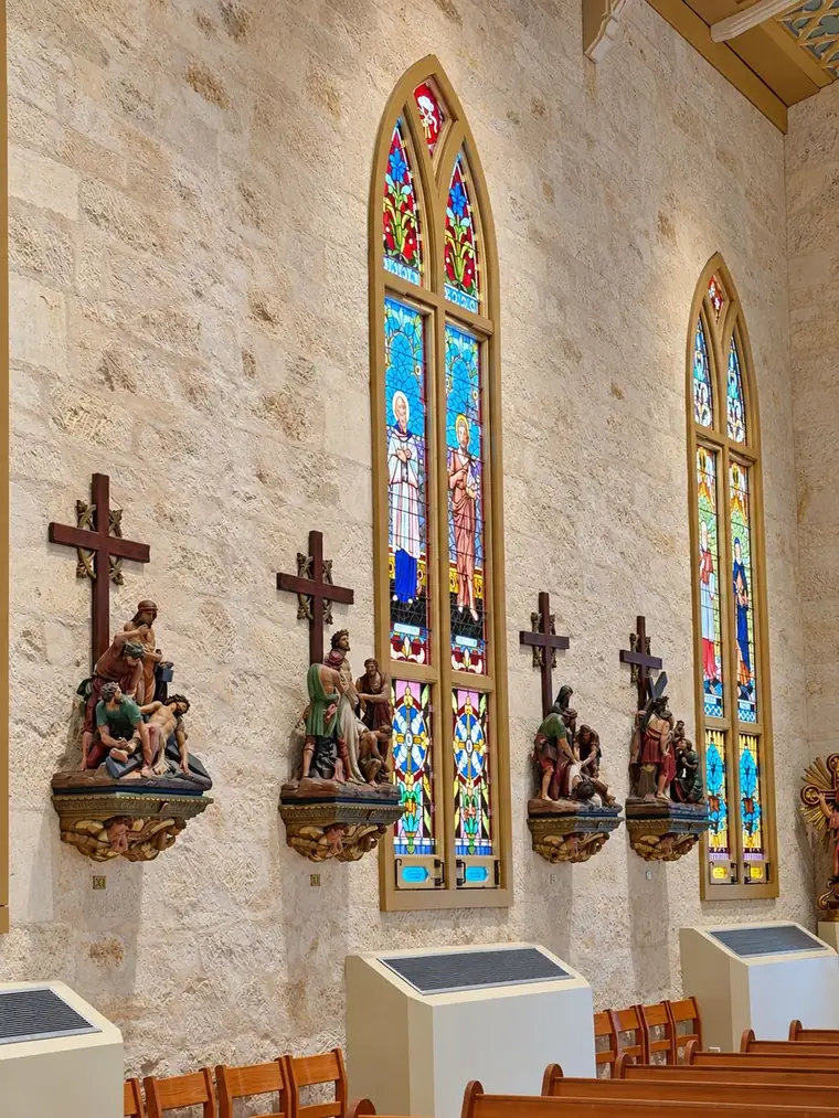 Four carved and painted Stations of the Cross mounted on gilt corbels along the limestone nave wall of San Fernando Cathedral, beneath tall stained glass lancets.